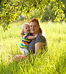 Woman in field of grass carrying a small child with a disability