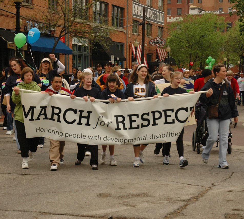 Teenagers walking in the March for Respect holding a banner that says, "Honoring people with developmental disabilities"
